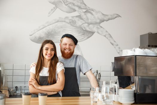 Coffee Business Concept - Positive young bearded man and beautiful attractive lady barista couple enjoy working together at the modern coffee shop