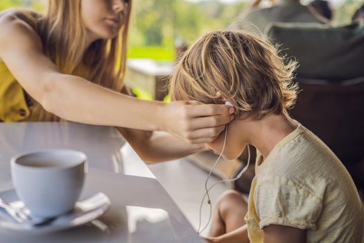 Mom puts her son in headphones in a cafe.