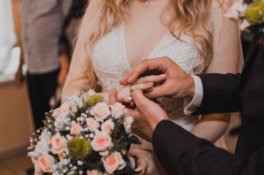 The bride and groom exchange rings. A man puts a wedding ring on a woman's hand. The girl put ring on man.