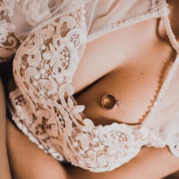 On the chest of the bride in a wedding white lace dress is a ring. Ring on a woman's breasts.
