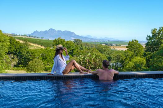 couple man and women in swimming pool looking out over the Vineyards and mountains of Stellenbosch South Africa.