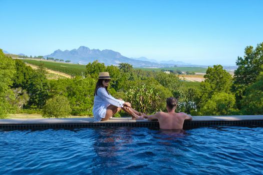 couple man and women in swimming pool looking out over the Vineyards and mountains of Stellenbosch South Africa.