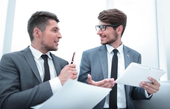 successful young businessmen look at each other and talk at the office. They use a tablet and paper for information