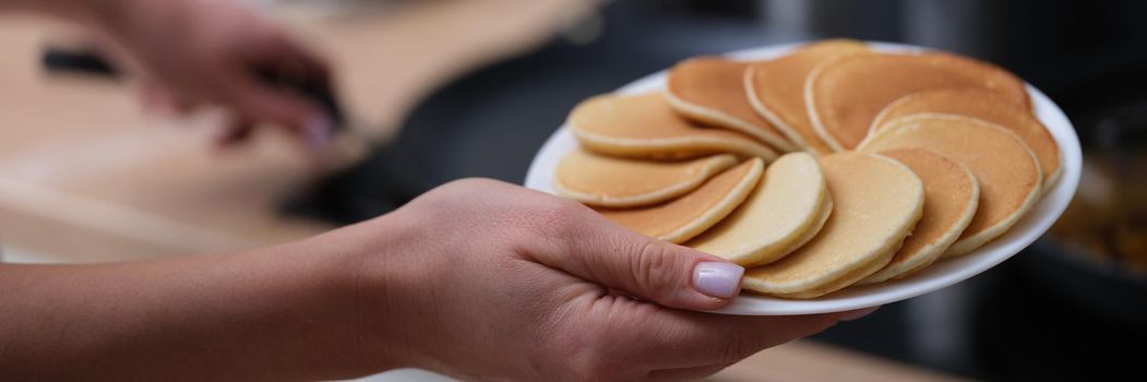 Woman holding plate of pancakes near stove in kitchen closeup. Rustic cuisine concept