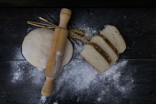 stick with wheat flour dough and slices of bread on rustic wood.
