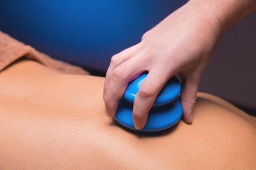 Close-up of a man's back with rubber vacuum cans installed in a dark room of a spa salon.