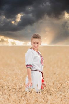 girl in an embroidered shirt on a wheat field and a sunset sky