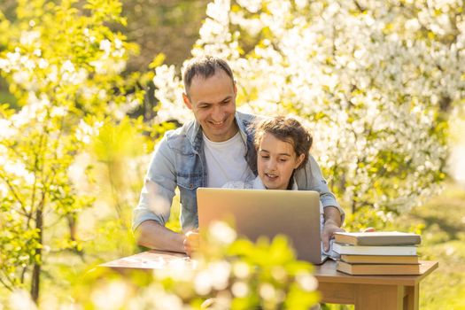 Caring young father helps little daughter, studying together watch online lesson on laptop, attentive dad and small girl child learning at home, have web class on computer on quarantine. outdoor.