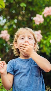 Boy blowing nose in front of blooming tree. Spring allergy concept. Children's allergies. VERTICAL FORMAT for Instagram mobile story or stories size. Mobile wallpaper