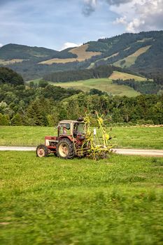 Agricultural machinery, a tractor collecting grass in a field against a blue sky. Season harvesting, grass, agricultural land. Selective focus