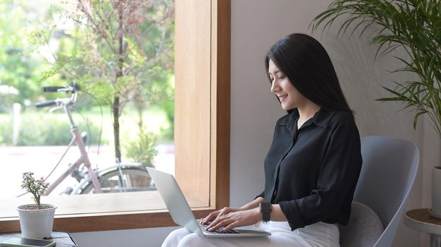 Attractive asian woman sitting in contemporary coffee shop and using laptop computer.