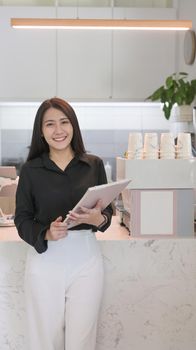 Portrait of female entrepreneur standing behind counter of coffee shop and smiling to camera.