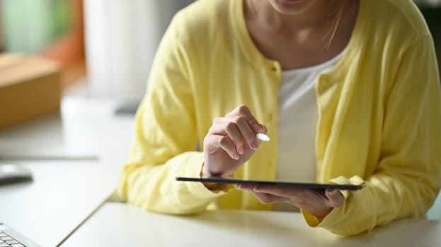 Cropped shot creative woman in casual clothes working at home and using digital tablet.