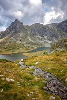 A mountain brook among stones flow to the lake. Vertical view