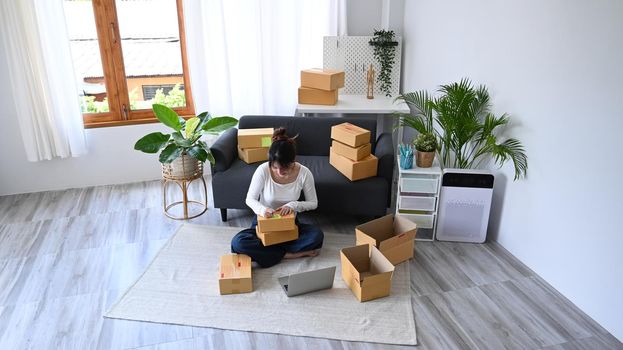 From above view young female online seller preparing parcel boxes of product for delivery to customers. E-commerce, Online selling concept.