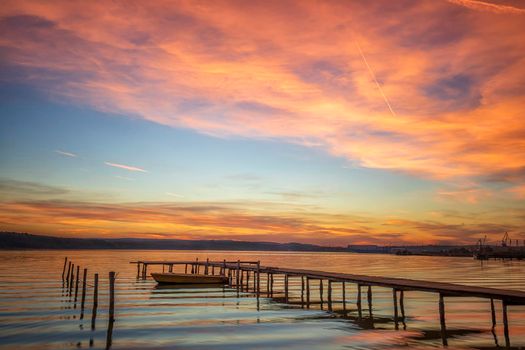 Magnificent sunset at the seashore with wooden pier and boat.