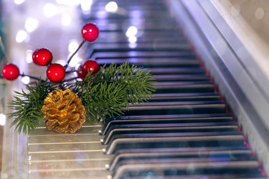 piano keys with golden pine cone, christmas tree branch and red berries on bokeh background. New Year or Christmas music concept. Soft focus