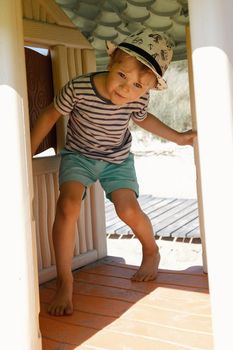 A little boy in a striped shirt in a small plastic playhouse on the beach