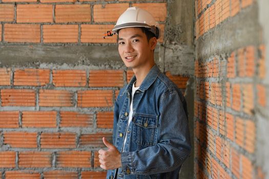 Asian architect man in safety helmet standing at construction site and smiling to camera. Industry, Engineer, construction concept.