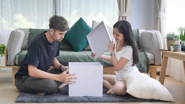 Young couple unpacking cardboard boxes in living room. Relocation house renovation, removals concept.