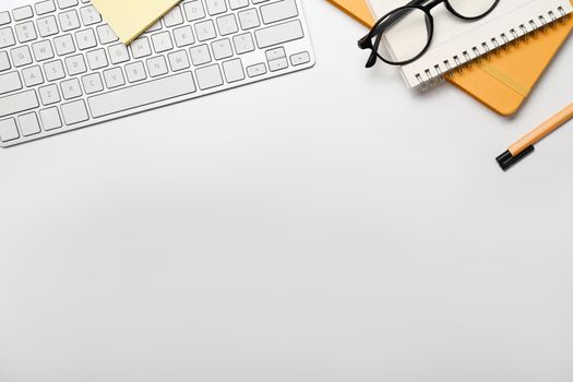 Flat lay wireless keyboard, notebook, eyeglasses and pen on white table. Copy space for your text.