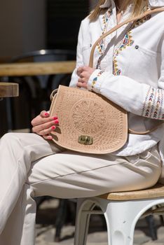 woman holds small beige women's leather bag with a carved pattern. Street photo