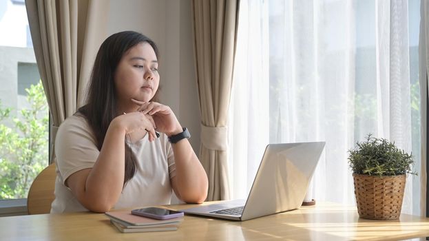 Thoughtful female freelancer working online with laptop computer at home.