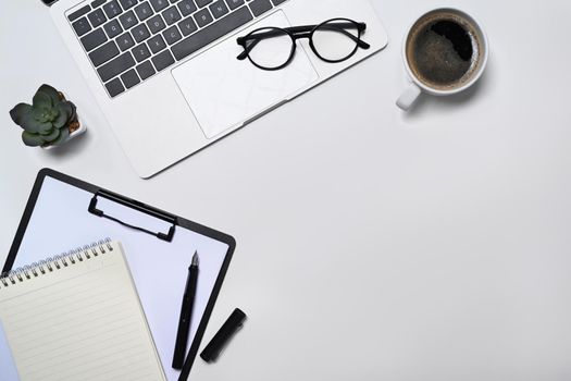 Computer laptop, eyeglasses, coffee cup, notebook and succulent plant on white office desk. Flat lay, Top view.
