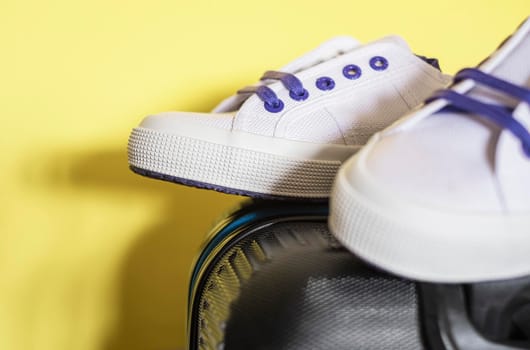Close up of a suitcase and white sneakers on a yellow background. Travel concept