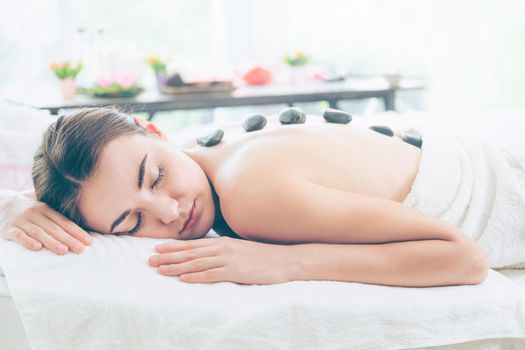 Woman getting hot stone massage treatment by professional beautician therapist in spa salon. Luxury wellness, back stress relief and rejuvenation concept.