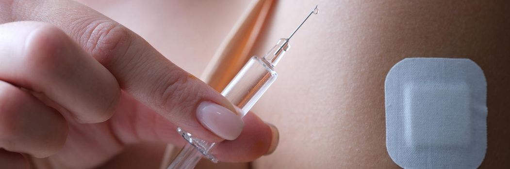 A woman holds a syringe with a medication, close-up. Beauty injections, plaster on the arm. Virus vaccine