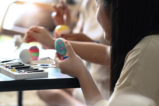Asian girl sitting in living room and enjoy painting water colors on eggs for Easter festival.