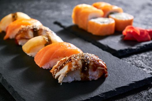 Assorted sushi with salmon, eel and escolar on black stone plate on dark background.