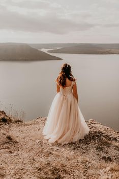 beautiful young brunette bride in a white wedding dress with a crown on her head stands on a cliff against the background of the river and islands.style fashionable women hairstyle makeup