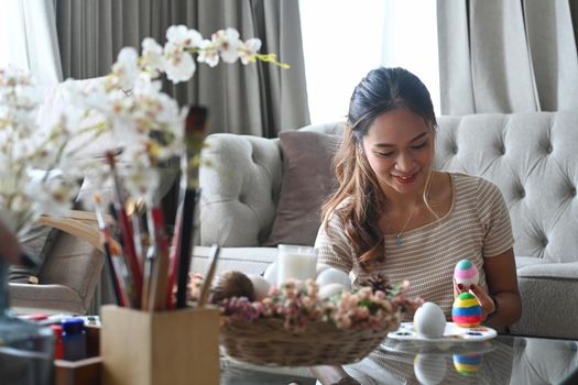 Charming woman enjoy painting eggs for Easter festival at home.