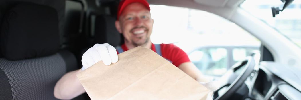 Joyful male courier gives a box while sitting in the car, delivering mail. Transportation of goods in the city, distribution