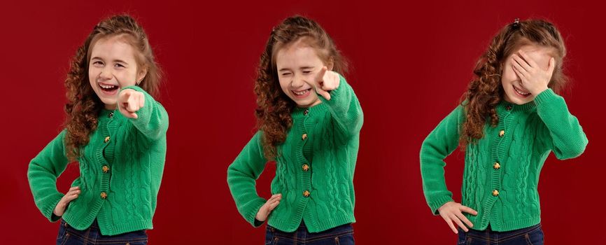 Close-up portrait of a lovely curly kid in a green knitted sweater laughing at someone while posing on a red studio background. Set of people sincere emotions, lifestyle concept. Mockup copy space.