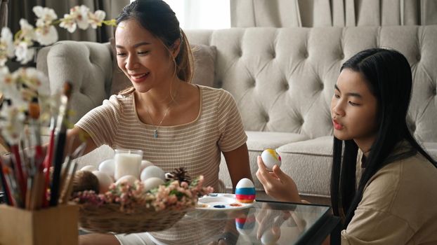 Loving young mother and her daughter painting Easter eggs together. Easter holidays and people concept.