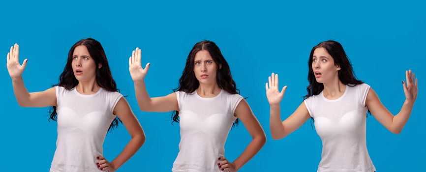 Close-up shot of a beautiful brunette woman in a white casual t-shirt posing against a blue studio background. She act like she is confused and trying to stop someone. Set of a people sincere emotions. Copy space.