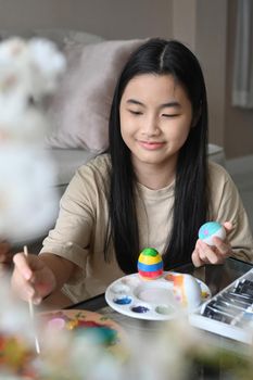 Cute little girl sitting in living room and enjoy painting on eggs for Easter festival.