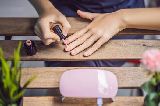 Young woman makes manicure with gel polish and UV lamp in pink shades.