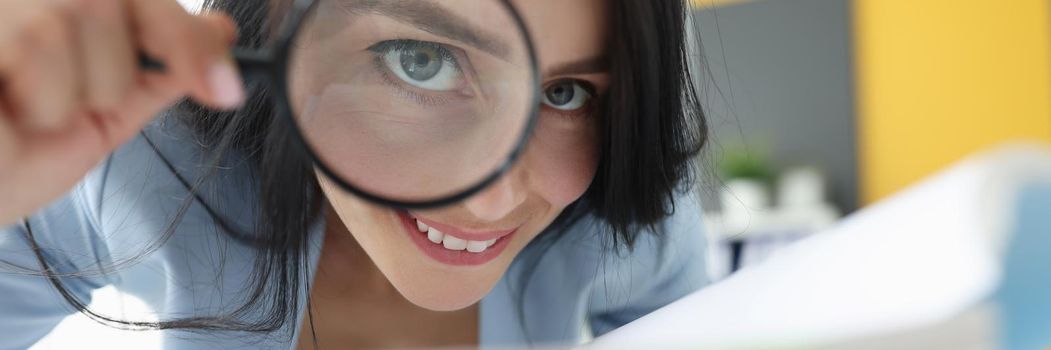 Joyful woman looks through a magnifying glass, close-up. Financial audit, detective agency, investigation, document archiving