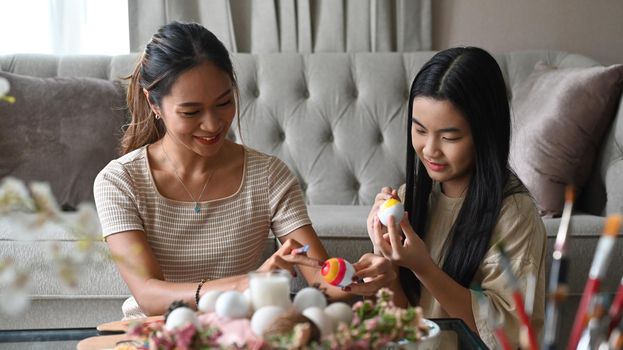 Beautiful asian mother and her daughter celebrating Easter festival, painting eggs together. Easter holidays concept.