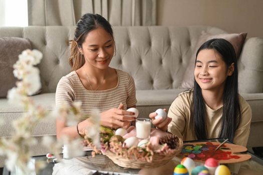 Joyful cute girl and mother painting Easter eggs preparing for Easter festival. Easter, holidays and people concept.