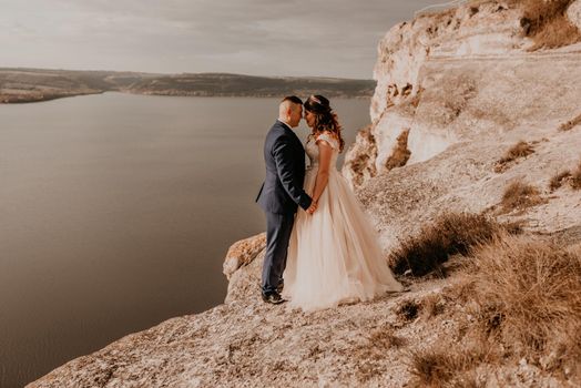 loving couple wedding newlyweds in white dress and suit walk in summer on mountain above river. sunset and sunrise. man and woman on rocks above cliff