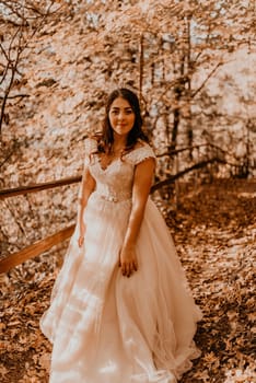 woman bride in white wedding dress with hairstyle makeup and crown on her head walks through autumn forest on fallen orange leaves