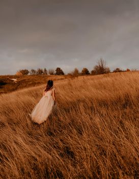 beautiful woman brunette bride in white dress and suit are walking on tall grass in field in summer