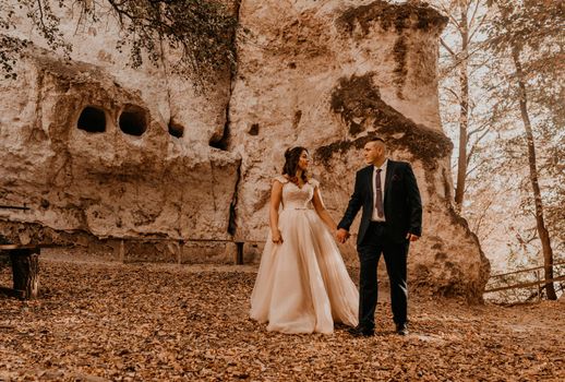 wedding couple in love man and woman walking autumn forest against background of stone rocks. groom suit and bride dress with crown on his head with haircut outdoors. rock monastery bakota