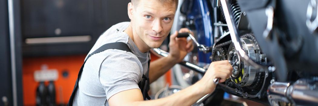 A male mechanic in uniform in a garage repairs a motorcycle. Inspection and diagnostics of a motorbike before the race
