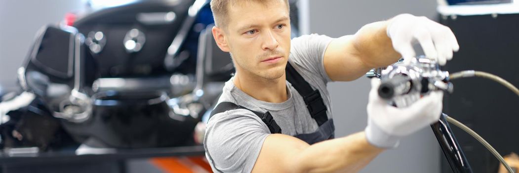 A male racer in the garage is changing motorcycle parts, close-up. Moto club bikers, repair in the garage after the race